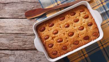 Basbousa in tray with wooden spoon next to the tray on a wooden table background